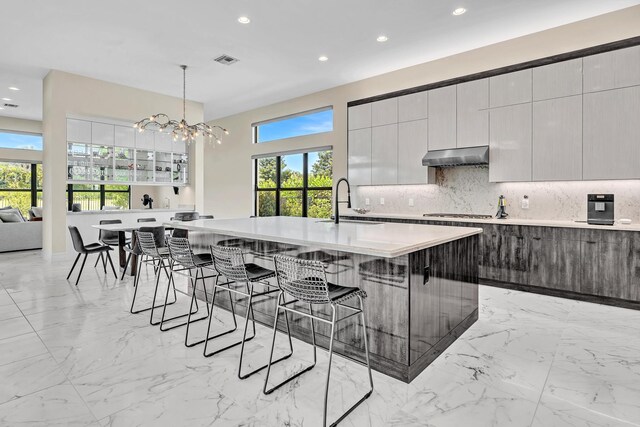 kitchen with decorative light fixtures, a kitchen breakfast bar, light tile patterned floors, and a kitchen island with sink