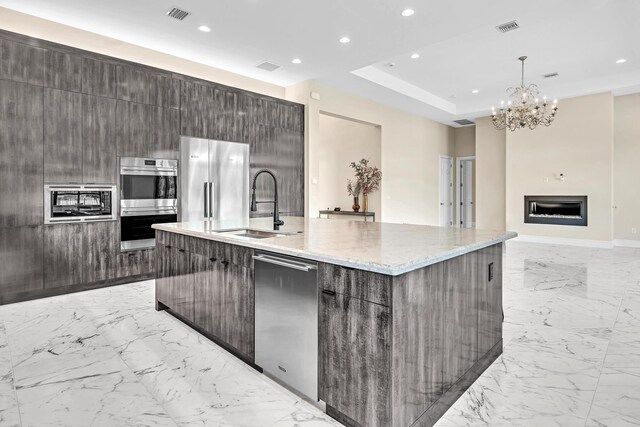 kitchen with light stone counters, sink, an island with sink, appliances with stainless steel finishes, and light tile patterned flooring