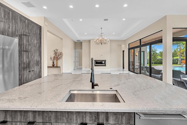 kitchen featuring a notable chandelier, light stone counters, an island with sink, and sink