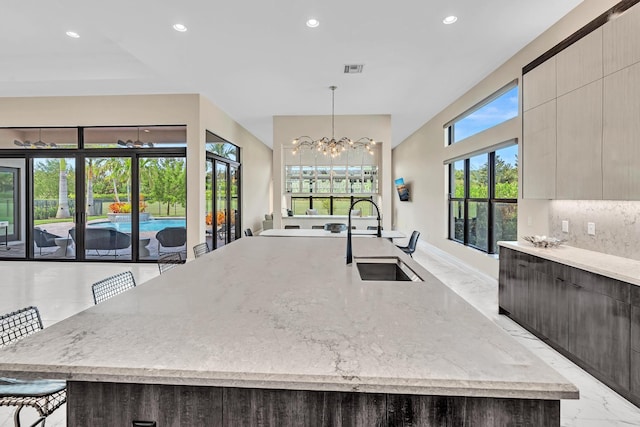 kitchen with a large island, modern cabinets, light stone countertops, marble finish floor, and a sink