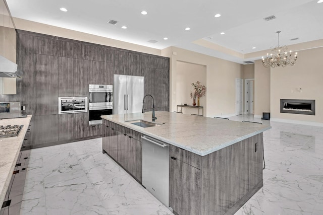 kitchen with light stone countertops, appliances with stainless steel finishes, sink, a large island with sink, and light tile patterned flooring