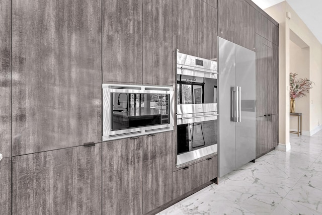 kitchen featuring marble finish floor, modern cabinets, baseboards, and stainless steel appliances