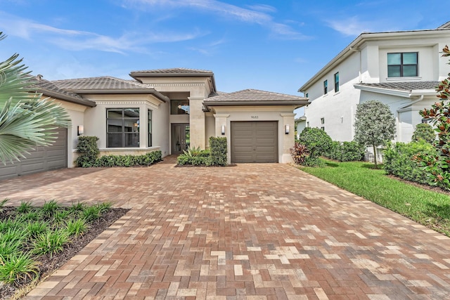 prairie-style home featuring a garage, decorative driveway, a tile roof, and stucco siding