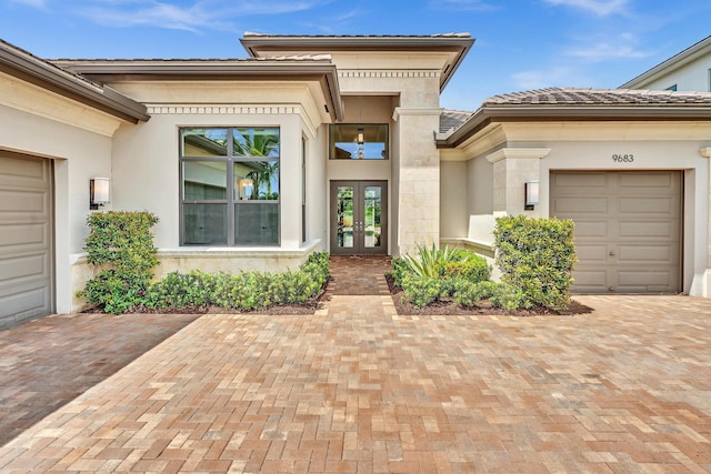 doorway to property with a garage, french doors, decorative driveway, and stucco siding