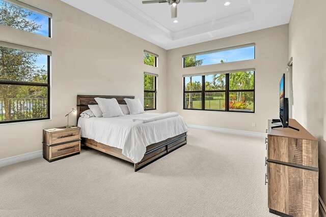 carpeted bedroom featuring a tray ceiling, a high ceiling, and ceiling fan