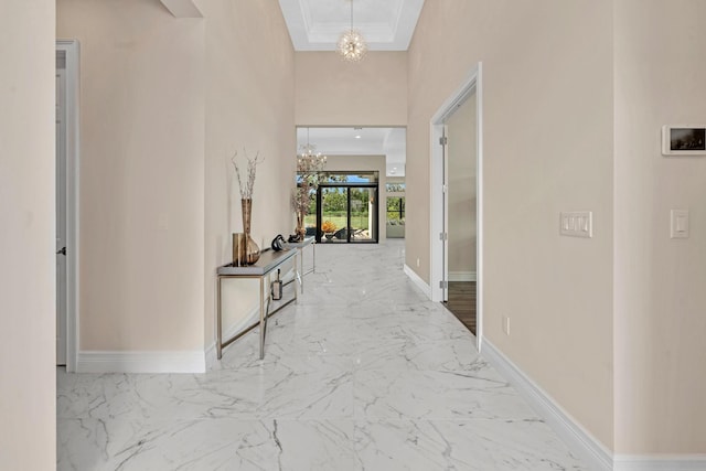 corridor featuring an inviting chandelier, baseboards, and marble finish floor