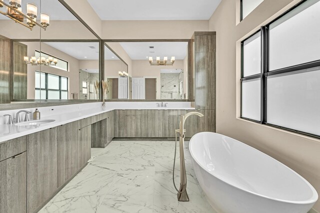 full bath with double vanity, an inviting chandelier, marble finish floor, a freestanding tub, and a sink