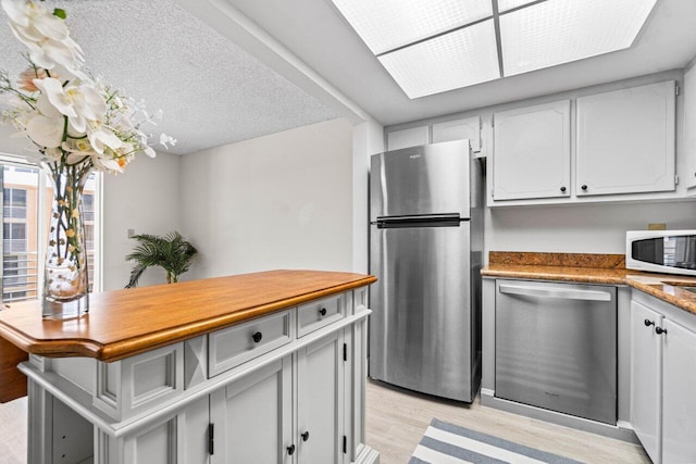 kitchen featuring white cabinetry, light wood-type flooring, a textured ceiling, and appliances with stainless steel finishes