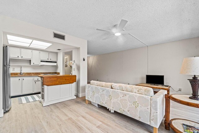 living room with ceiling fan, sink, light hardwood / wood-style floors, and a textured ceiling