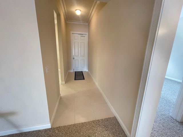 hallway featuring light colored carpet, baseboards, crown molding, and light tile patterned floors