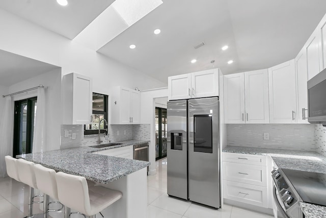 kitchen featuring white cabinetry, sink, stainless steel appliances, kitchen peninsula, and a breakfast bar