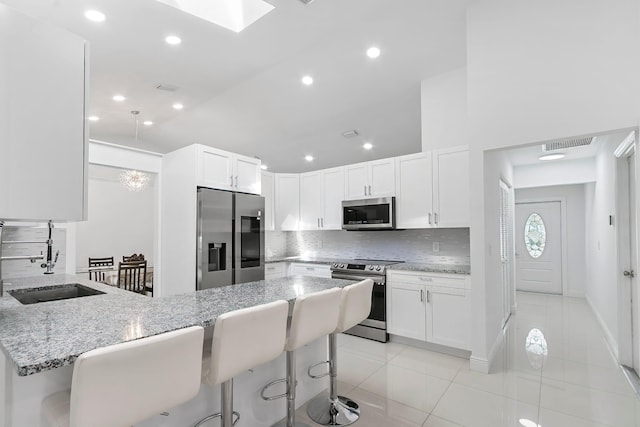 kitchen with stone counters, a breakfast bar, white cabinets, and stainless steel appliances