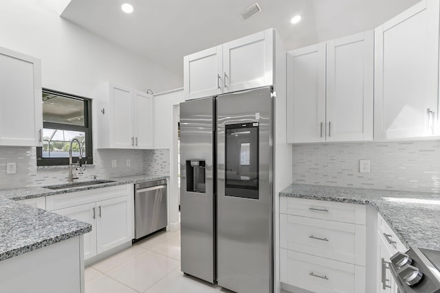 kitchen with stainless steel appliances, sink, light tile patterned floors, stone counters, and white cabinetry