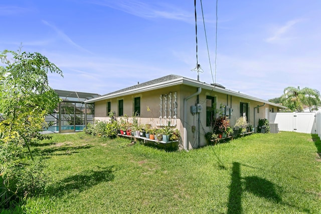 back of house featuring glass enclosure, central AC unit, and a lawn