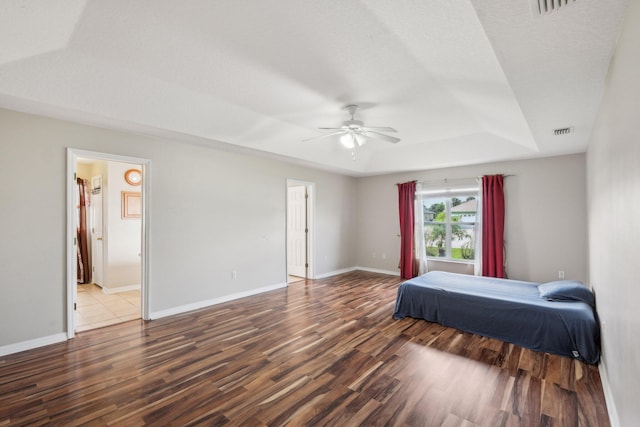 bedroom with a tray ceiling, wood-type flooring, connected bathroom, and ceiling fan