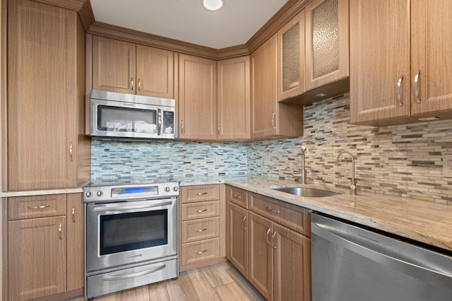 kitchen with light stone countertops, light wood-type flooring, stainless steel appliances, sink, and tasteful backsplash