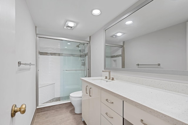 bathroom featuring wood-type flooring, a shower with shower door, toilet, and vanity