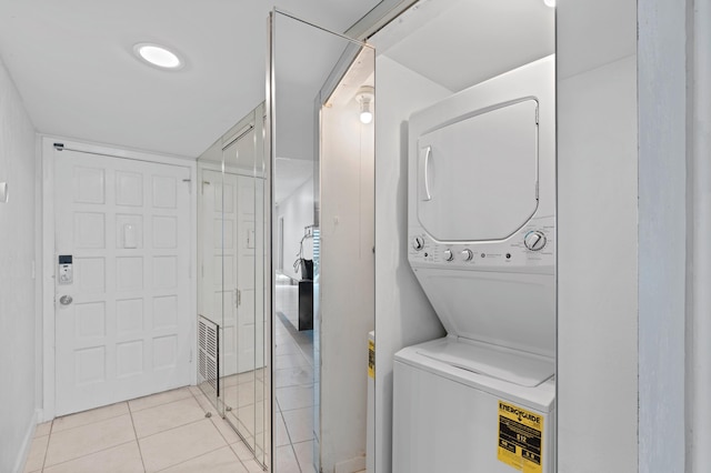 laundry room featuring stacked washer / drying machine and light tile floors