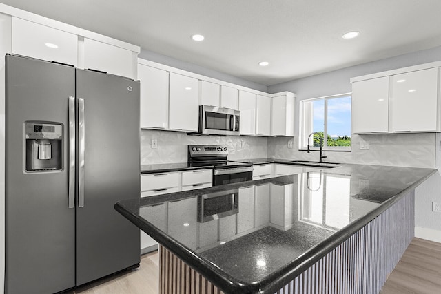 kitchen with light hardwood / wood-style floors, stainless steel appliances, white cabinets, sink, and tasteful backsplash