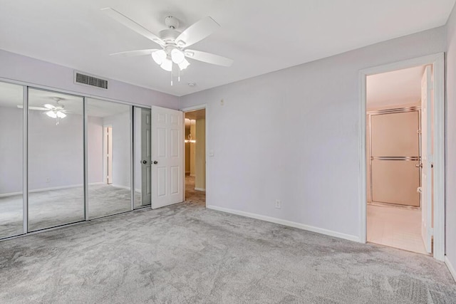 unfurnished bedroom with a closet, light colored carpet, ceiling fan, and ensuite bathroom