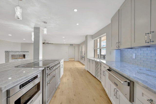 kitchen with a premium fireplace, light hardwood / wood-style flooring, tasteful backsplash, light stone countertops, and ceiling fan