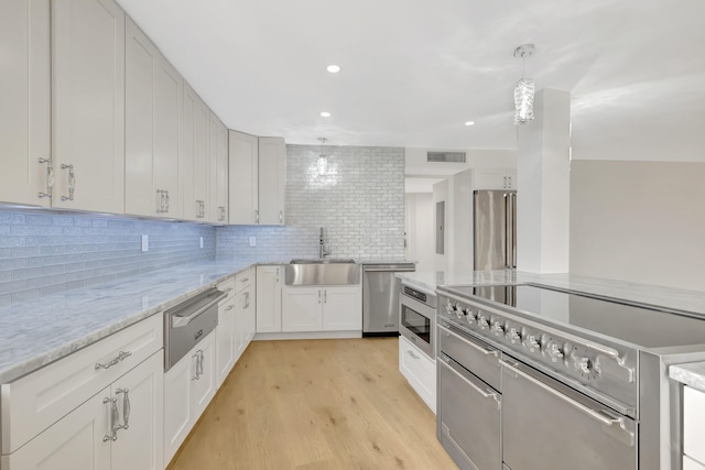 kitchen with white cabinetry, light wood-type flooring, decorative backsplash, high end appliances, and sink