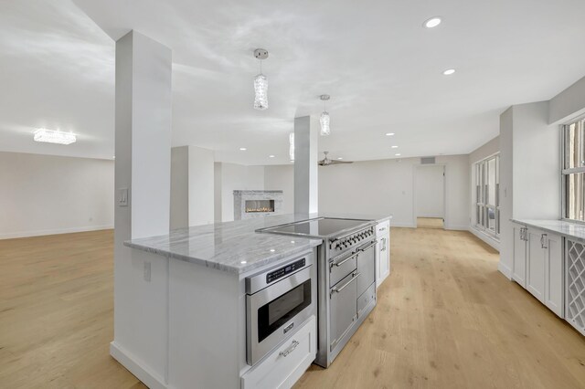 kitchen with white cabinets, light stone counters, wall oven, light hardwood / wood-style floors, and decorative light fixtures