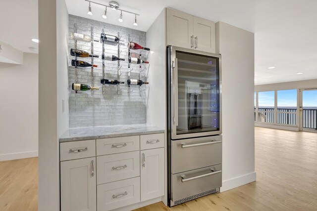 kitchen with light stone counters, light wood-type flooring, track lighting, and refrigerator