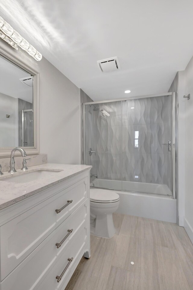 full bathroom featuring vanity, combined bath / shower with glass door, and toilet