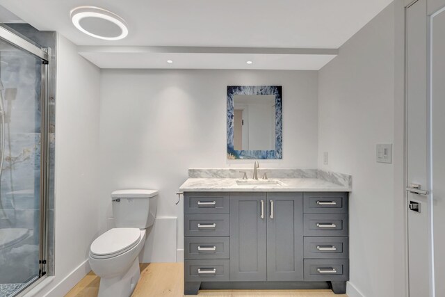 bathroom with a shower with shower door, vanity, wood-type flooring, and toilet