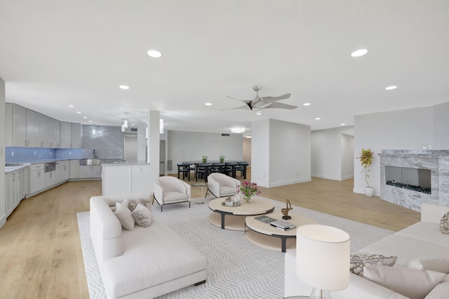 living room featuring ceiling fan, light wood-type flooring, and a high end fireplace