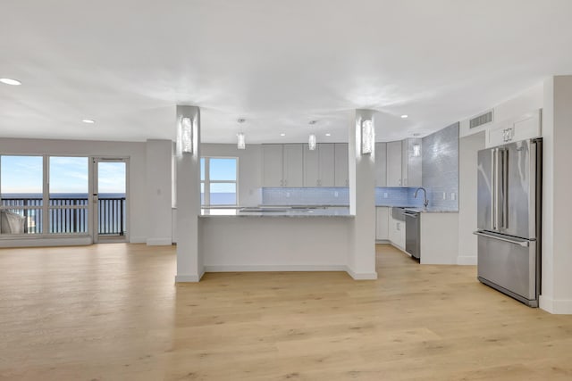 kitchen with stainless steel appliances, sink, light stone counters, backsplash, and light wood-type flooring