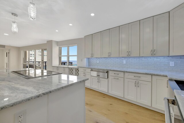 kitchen with stovetop, light stone counters, light hardwood / wood-style floors, decorative light fixtures, and decorative backsplash