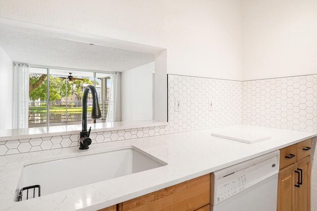 kitchen featuring light stone countertops, backsplash, white dishwasher, and sink