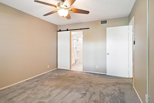 unfurnished bedroom with carpet, ensuite bathroom, a textured ceiling, ceiling fan, and a barn door