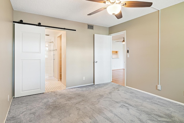 unfurnished bedroom with ceiling fan, a barn door, ensuite bathroom, light colored carpet, and a textured ceiling