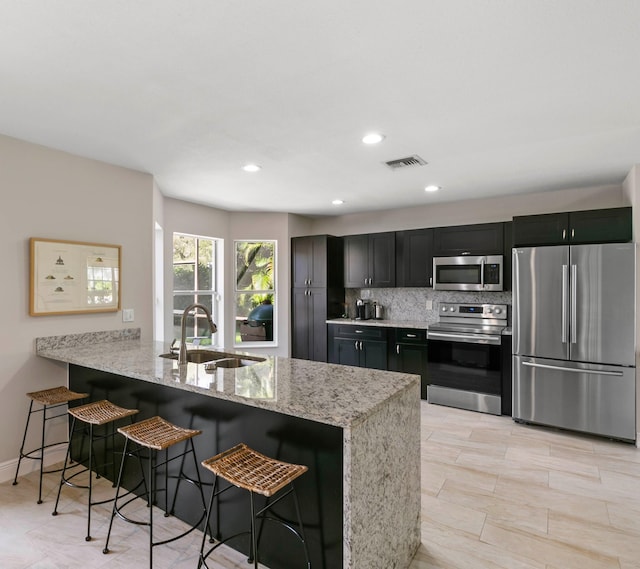 kitchen featuring appliances with stainless steel finishes, sink, light stone countertops, and a kitchen breakfast bar