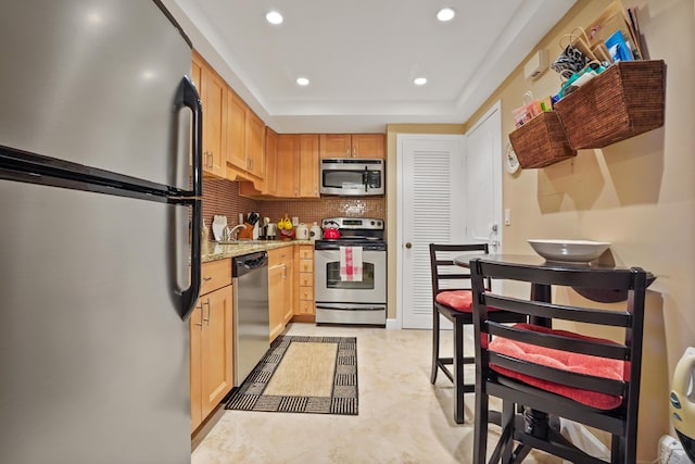 kitchen featuring sink, stainless steel appliances, tasteful backsplash, light stone counters, and light brown cabinetry