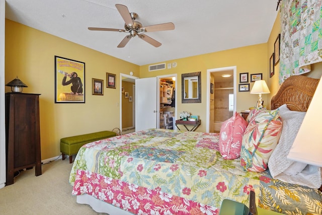 bedroom with a walk in closet, ensuite bathroom, light colored carpet, ceiling fan, and a closet