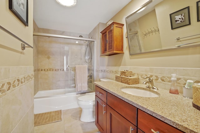 full bathroom with vanity, combined bath / shower with glass door, tile patterned flooring, toilet, and tile walls