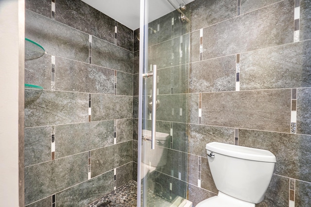 bathroom featuring tile walls, a shower with door, and toilet