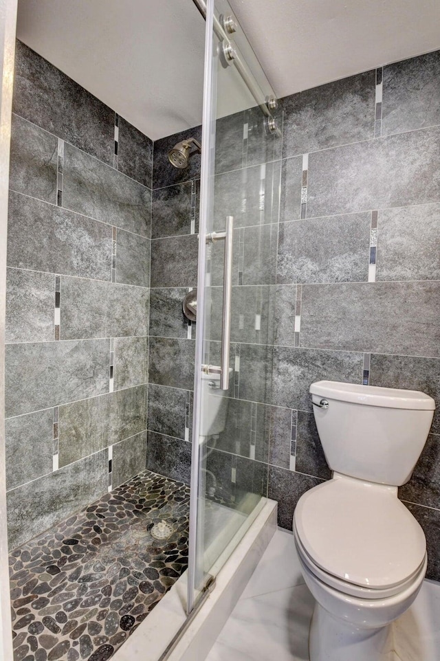 bathroom with tile walls, a shower with door, and toilet