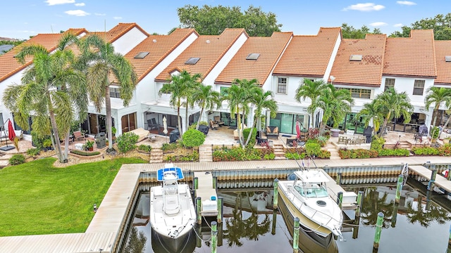 view of dock with a water view, a patio area, and a lawn