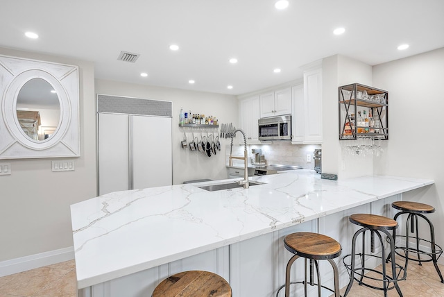 kitchen featuring white cabinets, a breakfast bar, kitchen peninsula, backsplash, and light tile patterned flooring