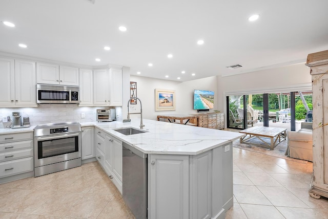 kitchen featuring light tile patterned floors, kitchen peninsula, stainless steel appliances, decorative backsplash, and sink