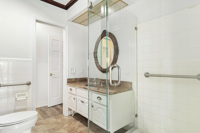 full bath featuring a shower with door, tile walls, crown molding, toilet, and vanity