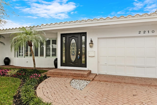 entrance to property with a garage, decorative driveway, a tile roof, and stucco siding