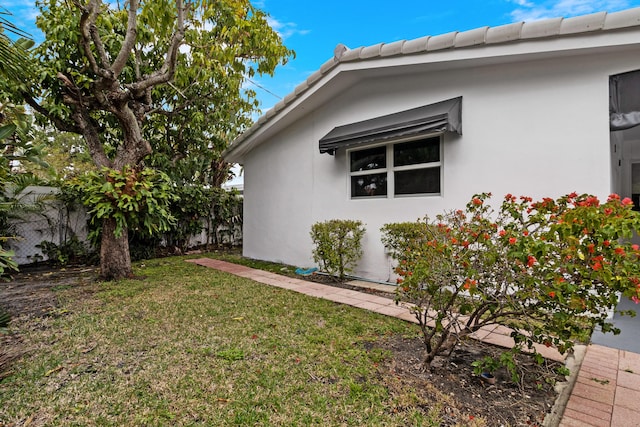 view of side of property with a yard, a tile roof, fence, and stucco siding