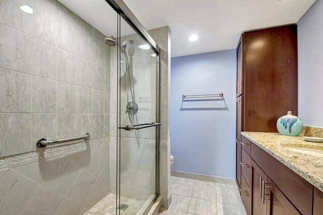 bathroom with tile floors, a shower with shower door, vanity, and toilet