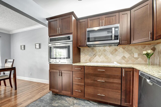 kitchen with dark hardwood / wood-style floors, light stone countertops, ornamental molding, and appliances with stainless steel finishes